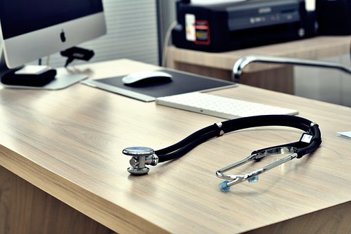 bureau d'un professionnel de santé avec un ordinateur, un souris et un stéthoscope sur la table - externaliser le secrétariat médical - Serenity